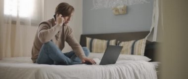 Evden bir dizüstü bilgisayarla çalışırken telefonla konuşan bir adam. Ağır çekim, BMPCC 4K