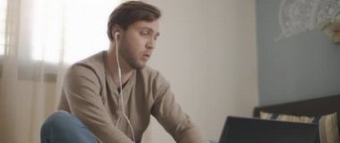 Laptopuyla uğraşırken kulaklıkla konuşan genç bir adam. Ev kavramından çalış. Ağır çekim, BMPCC 4K