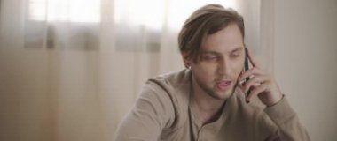 Evden bir dizüstü bilgisayarla çalışırken telefonla konuşan bir adam. Ağır çekim, yakın çekim. BMPCC 4K