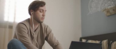 Laptopuyla uğraşırken kulaklıkla konuşan genç bir adam. Ev kavramından çalış. Ağır çekim, BMPCC 4K