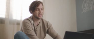 Laptopuyla uğraşırken kulaklıkla konuşan genç bir adam. Ev kavramından çalış. Ağır çekim, BMPCC 4K