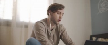 Laptopuyla uğraşırken kulaklıkla konuşan genç bir adam. Ev kavramından çalış. Ağır çekim, BMPCC 4K