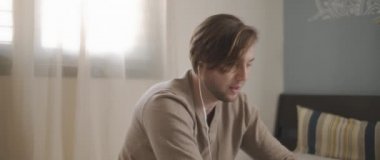 Laptopuyla uğraşırken kulaklıkla konuşan genç bir adam. Ev kavramından çalış. Ağır çekim, BMPCC 4K