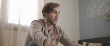 Laptopuyla uğraşırken kulaklıkla konuşan genç bir adam. Ev kavramından çalış. Ağır çekim, BMPCC 4K