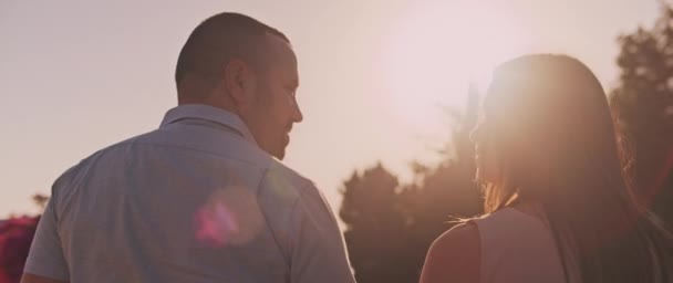 年轻夫妇面带微笑地望着对方 一边在日落时散步 一边回头看 美丽的太阳耀斑 慢动作 浅浅的Dof — 图库视频影像