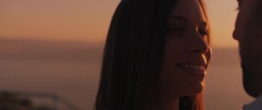 Gün batımında birbirlerine aşkla bakan genç bir çiftin arkasında güzel bir güneş parlaması. Yavaş çekim.  