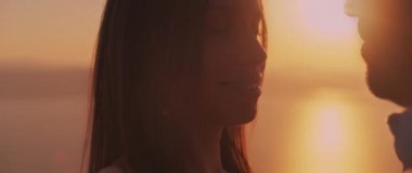 Gün batımında birbirlerine aşkla bakan genç bir çiftin arkasında güzel bir güneş parlaması. Yavaş çekim.  