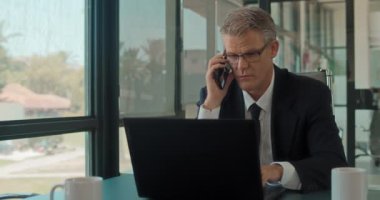 Ofiste dizüstü bilgisayarla çalışan bir iş adamı telefonda konuşuyor. Ortalama çekim, yavaş çekim. 