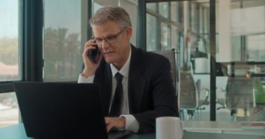 Ofiste dizüstü bilgisayarla çalışan bir iş adamı telefonda konuşuyor. Ortalama çekim, yavaş çekim. 