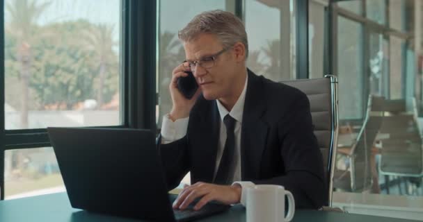 オフィスのノートパソコンで仕事をしている間に電話を切るビジネスマン スローモーションを追跡する — ストック動画