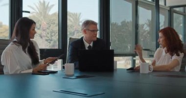 Üç kişilik bir grup bir iş projesini görüşmek için bir ofiste toplanıyor. Kendine güvenen, gülümseyen insanlar. İş toplantısı, birlikte çalışmak, fikir paylaşımı. Yavaş çekim.