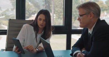 İki iş arkadaşı bir tablet kullanarak proje fikirlerini tartışıyor. İş toplantısı, birlikte çalışmak, fikir paylaşımı. Yavaş çekim.