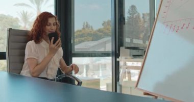 Genç bir iş kadınının ofisinde otururken bir telefon görüşmesini sonlandırdığı orta boy bir fotoğraf. Yavaş çekim.