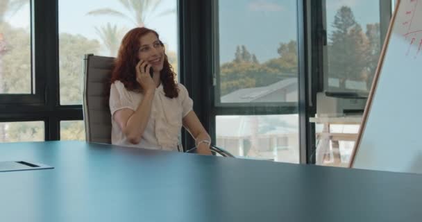 Bir Kadını Ofisinde Bir Sandalyede Otururken Biriyle Telefonda Konuşuyor Gülümsüyor — Stok video