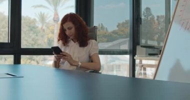 Ofisinde otururken telefonunu kullanan genç bir iş kadını. Yavaş çekim.