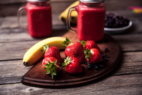 Smoothie with banana and strawberry in the glass, fresh strawberries and bananas on the old wooden background — Stock Photo, Image