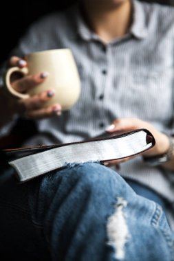 Bir kitap okuma ve fincan çay ya da kahve tutan genç kadın.