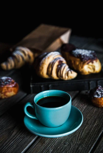 Croissant och vit kopp svart kaffe på brun duk. — Stockfoto