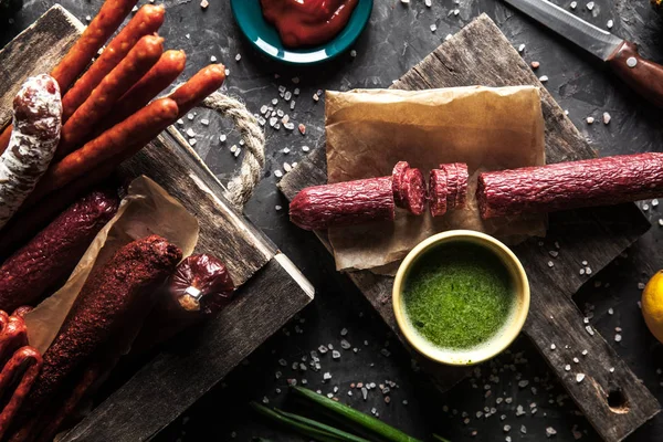 Колбаса на темном фоне с элементами приготовления пищи. Огурец, лук, кетчуп — стоковое фото