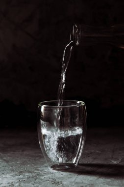 Şişeden siyah bir arka plan üzerinde cam bir bardağa dökülen su