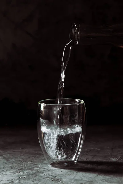 Agua vertida de la botella en una taza de vidrio sobre un fondo negro —  Fotos de Stock
