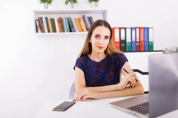 Masada oturan ve parlak ofisinde bir dizüstü bilgisayar kullanarak sevimli genç kadın