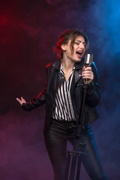 Portrait of expressive rock singer wearing leather jacket and keeping retro style microphone.