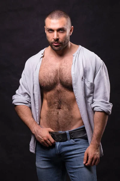 Acımasız kaslı adam, kot pantolon ve pamuklu gömlek. Ayakta rahatlatıcı vücut geliştirmeci.