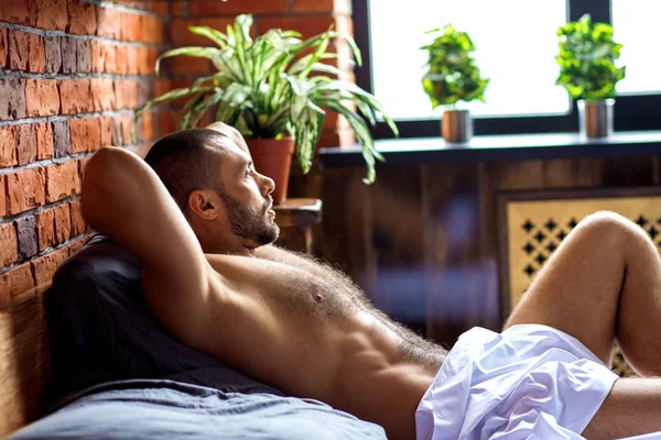Junges muskulöses männliches Model liegt im Bett und schaut zum Fenster. — Stockfoto