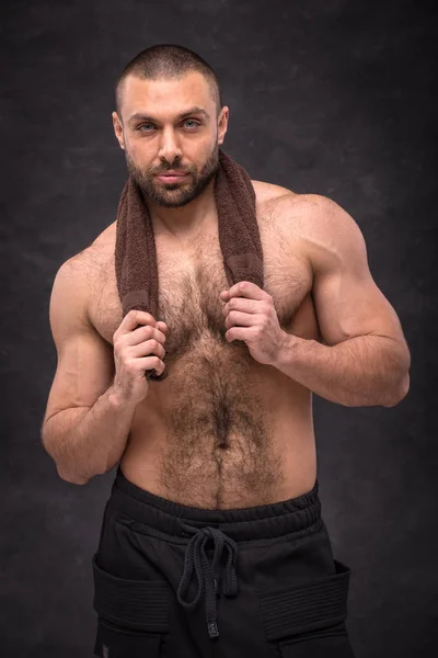Zor egzersiz eğitimden sonra dinlenme genç kaslı vücut geliştirmeci adam bir havlu ile poz.