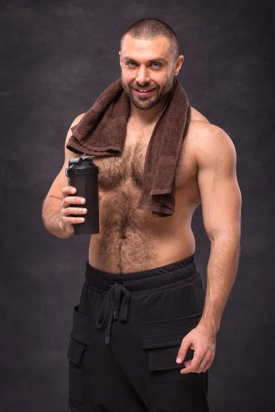 Genç kaslı vücut geliştirmeci adam eğitim, shaker siyah arka plan üzerine bir havlu ile poz sert bir çalışmadan sonra dinlenme