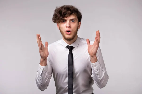 Hafif gri arka plan üzerinde şok duygusal yüz ifadesi ve eller jest ile genç adamın portresi
