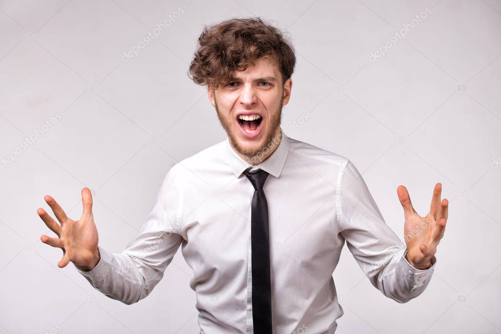 Angry furious businessman shouting out loud with hands up over gray background