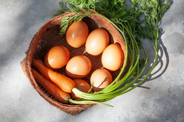 Carrots and eggs in a braided handmade basket, spotted cinnamon background.