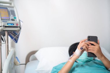 Genç kadın hasta hastane oyun smartphone intravenöz normal salin ile yatakta yatıyordu