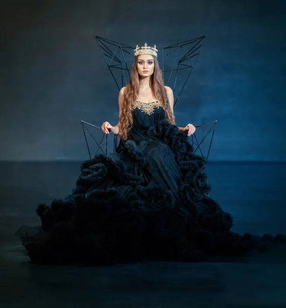 Model girl in a black dress and a crown on a throne of wire