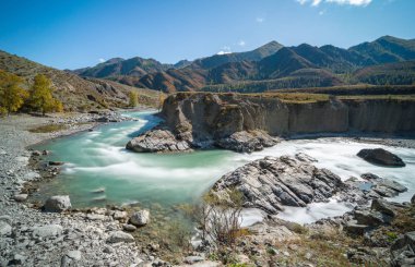 Sonbahar ağaçlarının arka planında bir dağ nehri