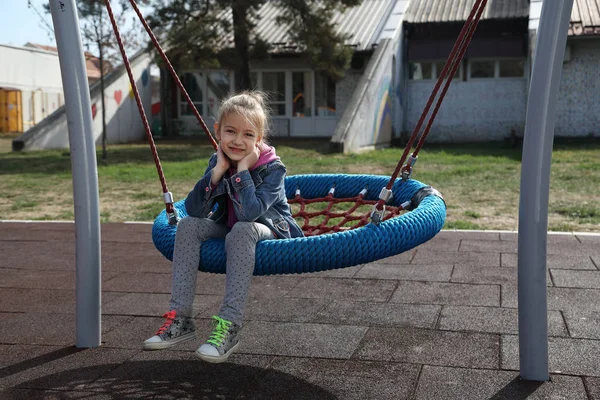 公園のブランコに座っているかわいい女の子が笑顔で晴れた秋の日にカメラを見て — ストック写真
