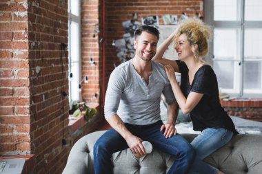 Güzel genç çift gülümseyen ve evde birlikte vakit süre kanepede oturan.