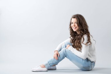 Gri arka plan üzerinde çapraz ayaklı katta oturan mutlu bir genç kadın. Genç.