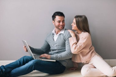 Genç mutlu çift katta oturan dizüstü bilgisayar kullanarak. Online alışveriş.