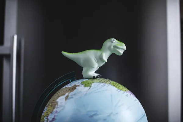 Tyrannosaurus dinosaurs toy on Globe model on dark background. Global warming and disaster concept.