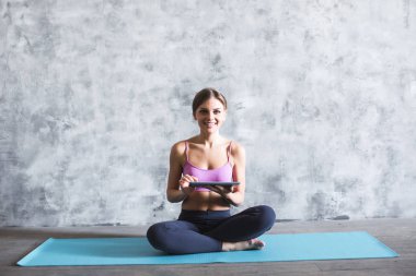 Spor salonunda bir yoga mat üzerinde elinde bir dijital tablet ile genç güzel kadın.