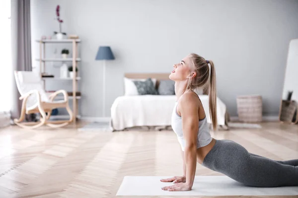 Ung sportig kvinna gör morgon övning i vardagsrummet på matta. — Stockfoto