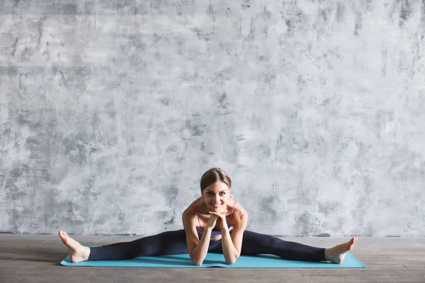 Joven hermosa mujer en ropa deportiva haciendo ejercicios de estiramiento en una esterilla de yoga en el gimnasio . — Foto de Stock