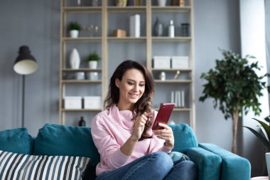 Evde akıllı telefon kullanan genç ve güzel bir kadın..