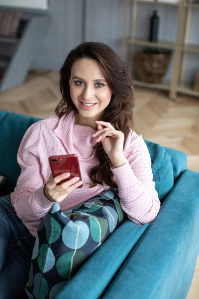 Happy woman using her smartphone on the couch at home in the living room. — Stock Photo, Image