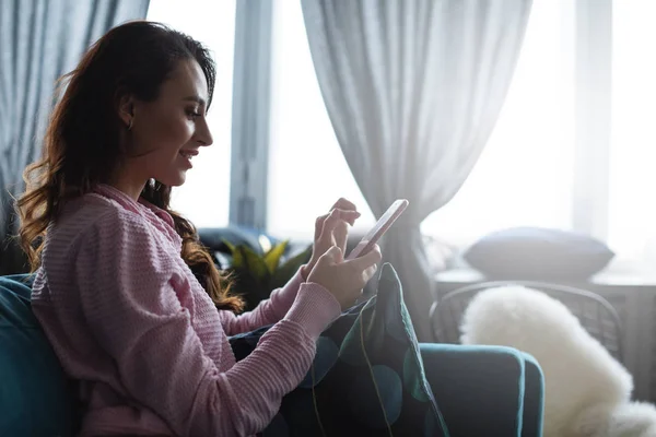 Mujer feliz usando su teléfono inteligente en el sofá en casa en la sala de estar . —  Fotos de Stock