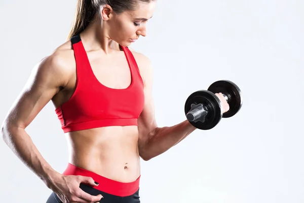 Fit vrouw met halters in sportkleding zwart-rood close-up. op een grijze achtergrond. — Stockfoto