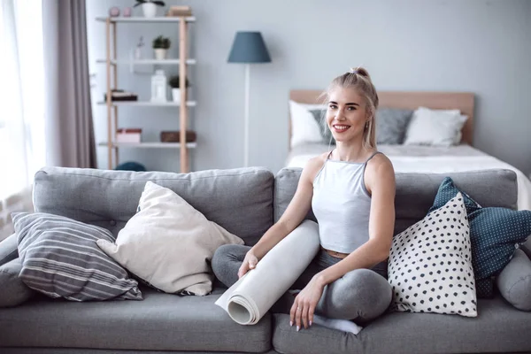 Kvinna med yogamatta som sitter på soffan i vardagsrummet hemma. — Stockfoto